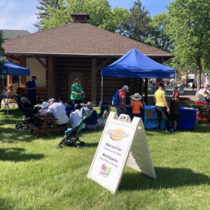 An outdoor scene with canopies, grass, and a signboard announcing "Make and Take" and "MathHappens" activities