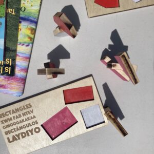 A multi-lingual rectangles puzzle, together with the chunky shapes for this puzzle and others. The shapes are stacked on their edges, and cast interesting shadows onto the surface beneath.
